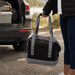 Premium 17L Foldable Cooler - A foldable cooler in black and grey, held by a person near the back of a vehicle. It has carrying straps and a logo.
