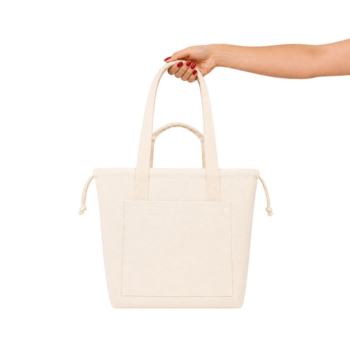 Darby Tote Bag - A cream tote bag with two handles and a front pocket, held by a hand with red nails. It has a logo.