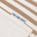 Hampton Tote Bag by The Line Edit. - A close-up of a striped tote bag in cream and tan, featuring a label with branding.