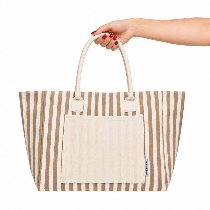 Hampton Tote Bag by The Line Edit. - A hand holds a striped brown and cream tote bag featuring a front pocket and dual handles.