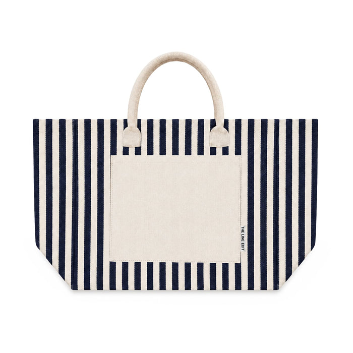 Hampton Tote Bag by The Line Edit. - A striped tote bag featuring navy blue and cream colours with two handles and a front pocket. It has a logo.