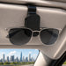 Visor Glasses Holder - A black visor glasses holder mounted on a car's sun visor, holding a pair of silver sunglasses.