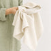 Haven Medium Cotton Tea Towel - A medium cotton tea towel in a natural beige shade held over a ceramic plate, featuring a subtle texture.
