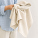 Haven Large Cotton Tea Towel - A large cotton tea towel in a light beige colour, held in one hand alongside a neutral-toned plate.