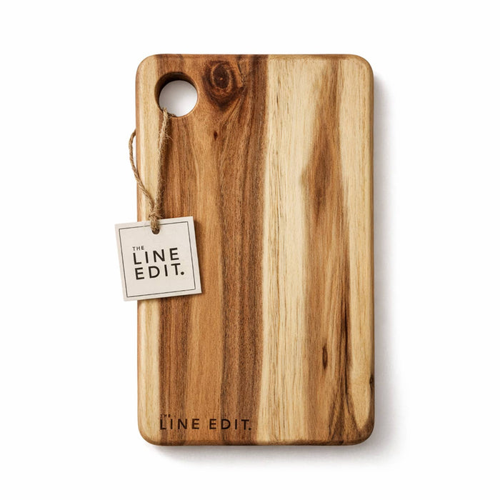 The Line Edit Acacia Serving Board - A wooden cheese board with a smooth finish, featuring natural wood grain and a tag for branding.