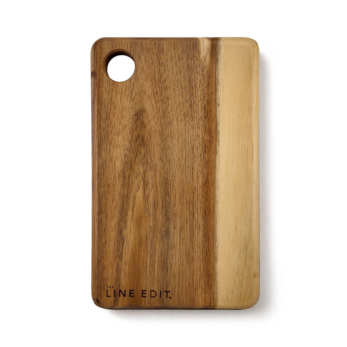 The Coastal Edit - An acacia serving board in warm brown tones, featuring a circular cut-out and a logo on the side.