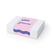 The Ultimate Welcome - Hot Chocolate Edition - A white box with pink and blue design featuring a logo. The text includes playful phrases and a wrap-around band.