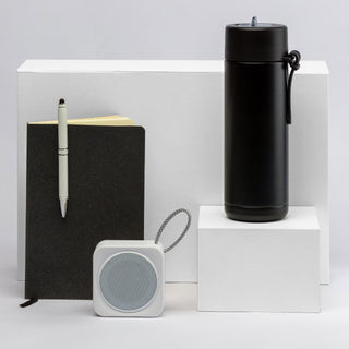 The Daily Setup - A black drink bottle, a black notebook, a white speaker, and a pen displayed on white pedestals.