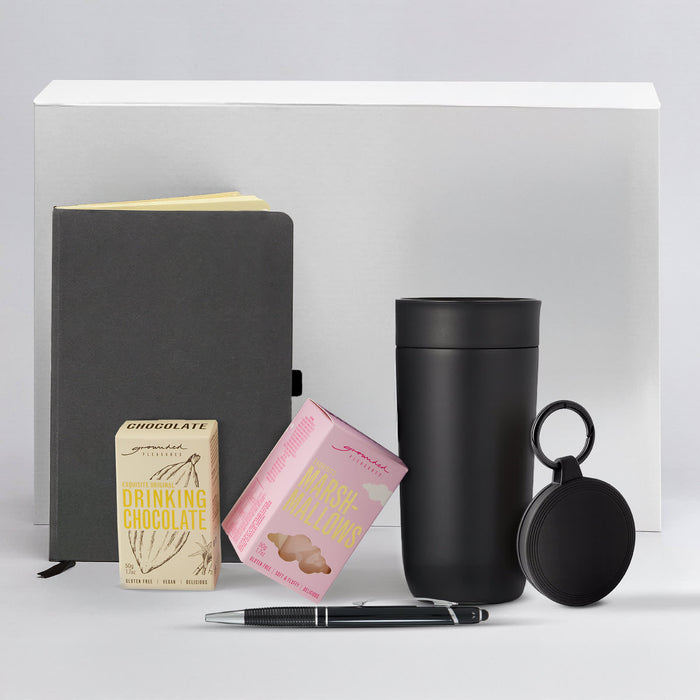 The Ultimate Welcome - Hot Chocolate Edition - A drink bottle, notebook, pen, and boxes of drinking chocolate and marshmallows in a monochrome setting.