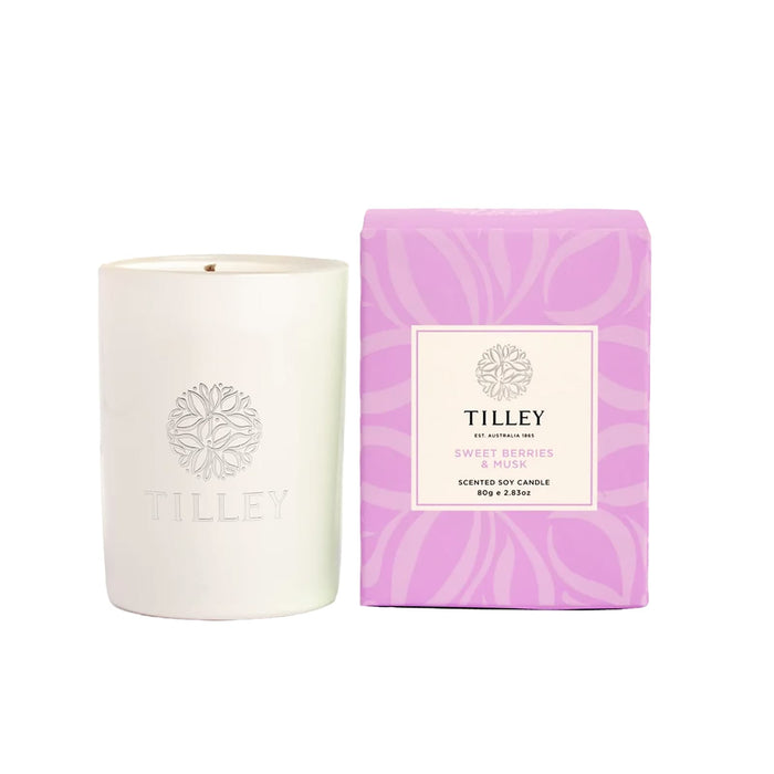 The Cosy Indulgence - A white scented soy candle is accompanied by a purple box, labelled "Sweet Berries & Musk", featuring a logo.