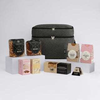The Good Things - A grey promotional bag surrounded by various snacks, including pretzels, beer nuts, caramel fudge, and coconut ice.