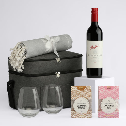 The Wine & Unwind - A drink bottle of red wine with two clear glasses, a grey blanket, and two packets of sweets in a stylish bag.