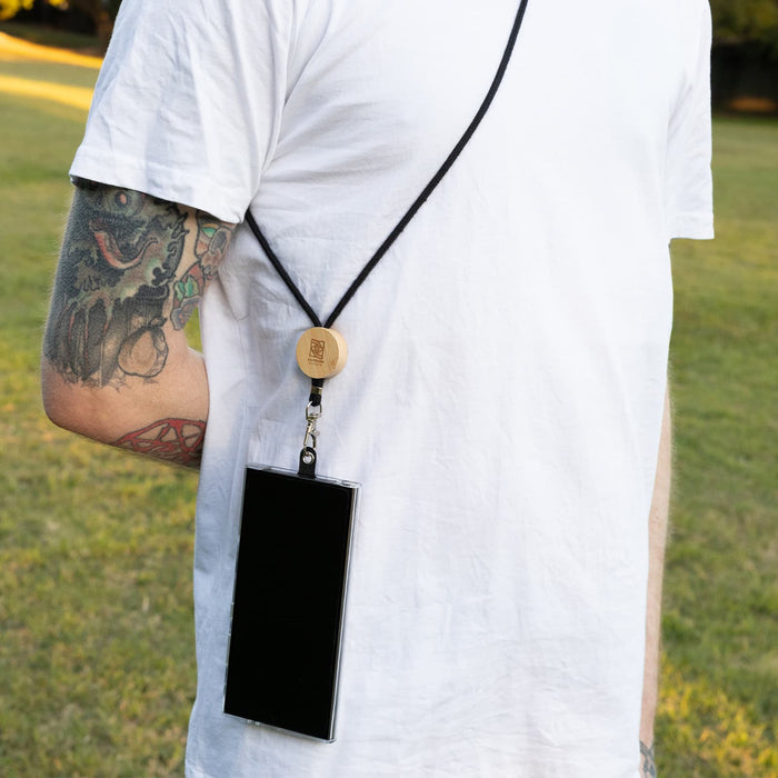 Shadow Phone Neck Lanyard - A black phone lanyard hangs from a wooden attachment, worn around the neck of a person in a field.