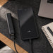 Symbolique 5,000mAh Power Bank - A black 5,000mAh power bank connected to a smartphone on a desk with a laptop and notebook.