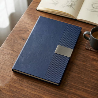 Vienna Notebook A5 - A navy blue A5 notebook with a textured cover and a silver clasp, placed on a wooden table next to a coffee cup.