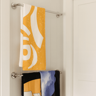 Bath Towel - A yellow bath towel with a pattern hangs above a black towel featuring a design, both on a towel rack.