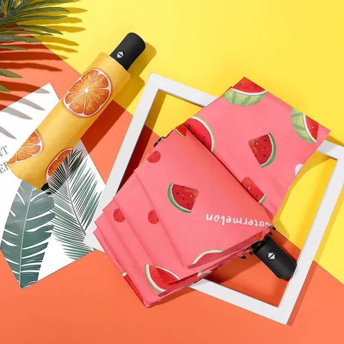 Full Colour Poppins Umbrella - A pink umbrella with watermelon patterns and a black handle, set against a bright yellow and orange background.