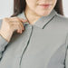 Women's Nevada L/S Micro Pique Polo - A close-up of a woman adjusting the collar of a grey long-sleeve polo shirt with buttons and a logo.