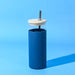 Sunrise Smoothie 500mL Tumbler - A drink bottle with a blue silicone exterior, wooden lid, and metal straw on a blue background.
