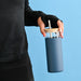 Sunrise Smoothie 500mL Tumbler - A drink bottle with a blue exterior, clear top, and bamboo lid, featuring a straw and held by a person.