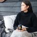 Zen Mirror Finish Mugs (350mL) - A drink mug with a Zen mirror finish in black, featuring a design, held by a person seated on a couch with cushions.