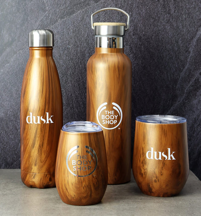 Ecograin Mirror Finish 230mL Calm Cup - A drink bottle and three cups in a wooden finish, featuring logos, against a dark textured background.