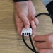 The Power Band Charging Lanyard - 60W - A black charging lanyard with a white connector, being adjusted in a person's hands on a wooden surface.