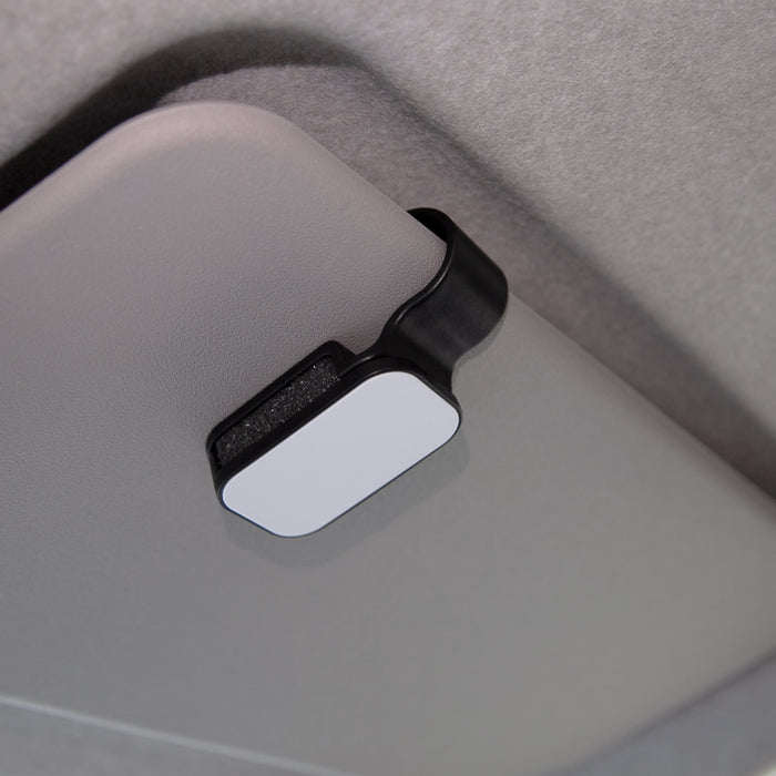 Car Visor Sunglass Holder - A car visor sunglass holder in black and white, mounted on a grey car interior. It has a simple, sleek design.