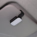 Car Visor Sunglass Holder - A car visor sunglass holder in black and white, mounted on a grey car interior. It has a simple, sleek design.