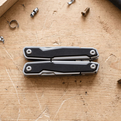 Trekk Multifunction Tool - A silver and black multifunction tool displayed on a wooden surface, surrounded by small screws and metal fragments.