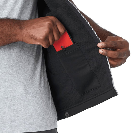Men's Joris Eco Waterproof Softshell Vest - A person's hand reaching into a pocket inside a grey softshell vest, featuring a black interior. The vest has a logo.