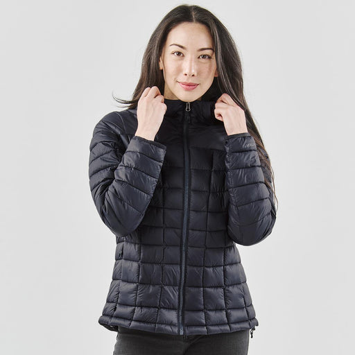 Women's Tundra Thermal Jacket - A woman wearing a black puffer jacket with a high collar, standing against a neutral background.