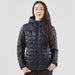 Women's Tundra Thermal Jacket - A woman is wearing a navy puffer jacket with a hood, featuring a quilted pattern and a front zipper.