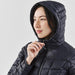 Women's Tundra Thermal Jacket - A woman wearing a navy puffer jacket with a hood, featuring a zipped front and quilted design.