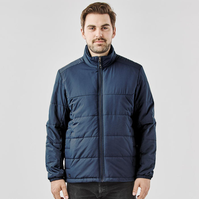 Men's Sierra Thermal Jacket - A man wearing a navy blue puffer jacket with a zippered front and a high collar. The jacket has a branded logo.