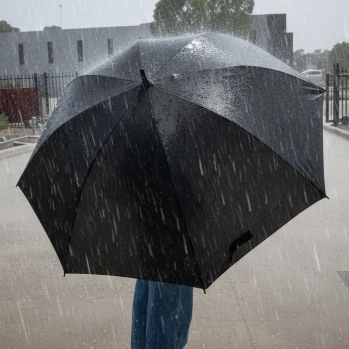 York Umbrella - A black umbrella in heavy rain, held by a person wearing blue jeans, with raindrops falling around it.