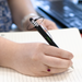 The Balance Pen - A black and silver pen with a unique balance design is held above a notebook with blank pages.